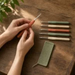 Hands holding one of six ergonomic crochet hooks, with the rest of the set and a bookmark (yarn not included)